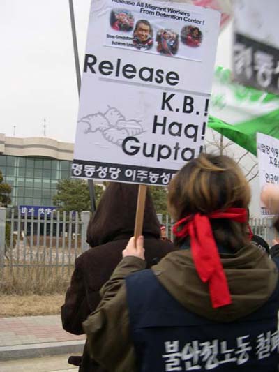 10일 화성외국인 보호소 앞 집회에서 한 시위자가 보호중인 샤말, 케비, 헉, 굽타씨의 사진이 든 안내판을 들고 있다. 